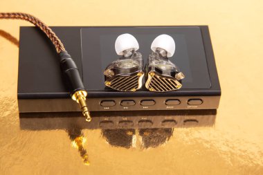 Kablolu kulaklıklar ve siyah bir ses çaların üzerinde örülmüş kablolar, altın bir yüzeye yansıyor. Teknoloji ürünleri ve müzik temaları için mükemmel..