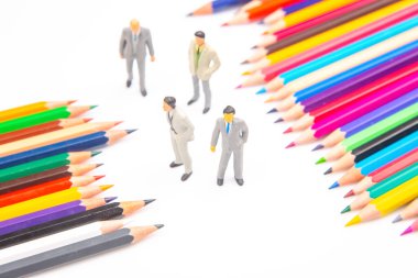 Canlı renkli kalemler beyaz arka planda fan şeklinde dizilmiş ve yanında yaratıcılık ve takım çalışmasını sembolize eden üç küçük iş adamı figürü bulunuyor. minyatür insanlar