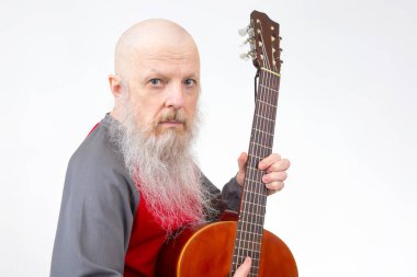 Beyaz sakallı kel bir son sınıf öğrencisi, akustik gitar çalıyor, kırmızı ve gri tişörtlü, beyaz tenli, müzikal ifade ve yaratıcılığın bir anını tasvir ediyor..