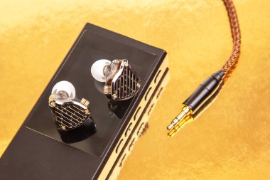 Sade siyah bir müzik çaların üzerinde örülmüş kabloyla kablolu kulaklıklar, altın bir yüzeye yansıyor. Teknoloji, ses ve minimalist tasarım stok fotoğrafçılığı için mükemmel..