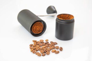 Siyah bir el yapımı kahve öğütücüsü, parçalanmış, içinde taze öğütülmüş kahve olduğunu ortaya çıkarıyor, temiz, minimalist bir görünüm için beyaz arka plana dökülen kahve tozu..