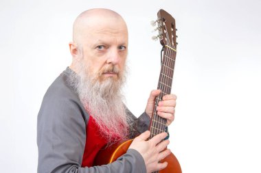 Beyaz sakallı kel bir son sınıf öğrencisi, akustik gitar çalıyor, kırmızı ve gri tişörtlü, beyaz tenli, müzikal ifade ve yaratıcılığın bir anını tasvir ediyor..