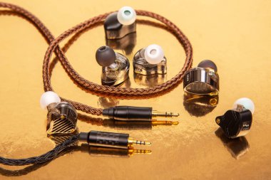 Üç kulaklık, dokuma kablo ve altın kaplamalı altın kaplama arka plan, ses teknolojisi ve ürün çekimleri için mükemmel..