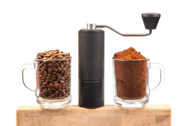 Bir el yapımı kahve öğütücüsü iki cam bardak arasında oturur, biri kavrulmuş kahve çekirdekleri, diğeri taze öğütülmüş, ahşap bir yüzeyde, kahve öğütme işlemini gözler önüne serer.