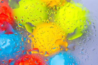 Yansıtıcı yüzeyde kırmızı, sarı, mavi ve yeşil renkli su damlacıkları, soyut fotoğrafçılık veya yaratıcı projeler için idealdir.