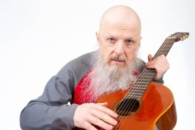 Uzun gri sakallı yaşlı bir adam, kırmızı ve gri spor gömlekli tahta bir gitarla beyaz bir arka plana karşı şarkı söylüyor ve müziğe olan sevgisini vurguluyor..