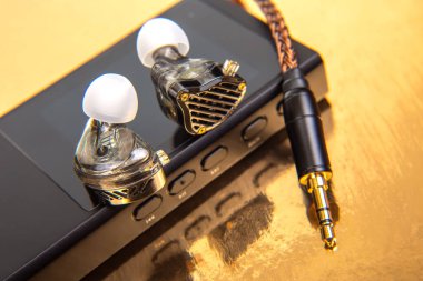 Kablolu kulaklıklar, siyah bir ses cihazına örülmüş, parlak altın bir arka planda ayarlanmış. Müzik severler, teknoloji meraklıları ve ürün çekimleri için ideal. Yüksek çözünürlüklü fotoğraf.