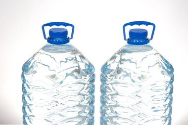 İki şeffaf su şişesi, mavi kapaklı ve desenli, beyaz bir yüzeye yerleştirilmiş. Hidrasyon, sağlıklı yaşam veya sürdürülebilir yaşam tarzı kavramlarını desteklemek için birebirdir..