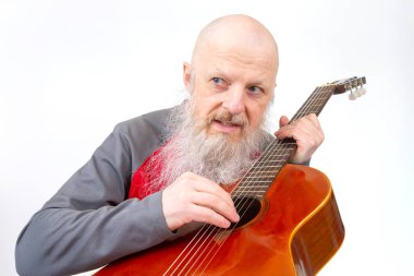 Uzun gri sakallı yaşlı bir adam, kırmızı ve gri spor gömlekli tahta bir gitarla beyaz bir arka plana karşı şarkı söylüyor ve müziğe olan sevgisini vurguluyor..