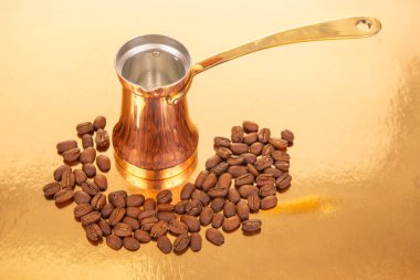 Kahve çekirdeğinin yanında altın saplı geleneksel bakır çakmak. Lüks altın bir yüzeye kurulmuş. Gurme kahve ve mutfak dekorları için ideal.