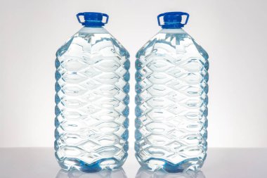 İki şeffaf su şişesi, mavi kapaklı ve desenli, beyaz bir yüzeye yerleştirilmiş. Hidrasyon, sağlıklı yaşam veya sürdürülebilir yaşam tarzı kavramlarını desteklemek için birebirdir..