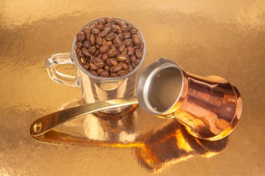 Pirinç saplı bakır bir kahve demliği ve altın kaplamalı kahve çekirdekleri ile dolu bir cam bardak. Sıcak bir mutfak, kültür ya da lüks mutfak eşyaları fotoğrafçılığı için idealdir.