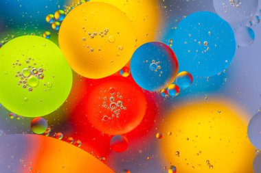 Pürüzsüz bir zemin üzerinde parlak kırmızı, sarı, mavi ve yeşil tonlarda su damlalarının çarpıcı soyut bir görüntüsü..