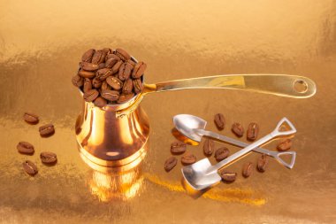 Işıl ışıl altın bir zemin üzerinde kavrulmuş kahve çekirdeklerinin yanında altın rengi kahve kabı bulunan şık bakır Türk kahve demliği, kahve geleneği ve mutfak resimleri için ideal.