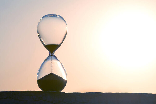 Hourglass framed by a radiant sunset, sand trickling down in soft light. Great for illustrating time, serenity, and nature. High-res image suitable for creative projects.