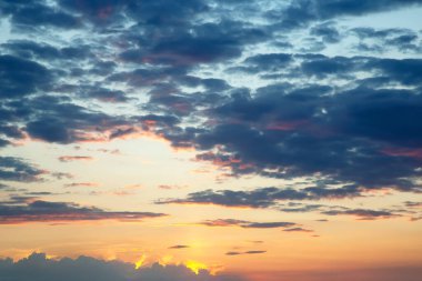 Karanlık ve aydınlık bulutlar çarpıcı bir günbatımı gökyüzünde harmanlanır. Güneşin altın parıltısı bulutların kenarlarını hafifçe aydınlatır, rüya gibi ve karamsar bir etki yaratır..