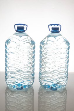 Mavi kapaklı ve desenli iki büyük plastik su şişesi beyaz arka planda yan yana duruyor. Susuzluk, sağlık ve çevre dostu temalar için mükemmel..
