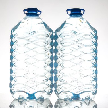 Dalgalı bir dokusu olan mavi kapaklı bir çift temiz plastik su şişesi, beyaz bir zemin üzerine kurulmuş. Sıvı, sağlık veya içecek stoku fotoğrafçılığı için ideal.