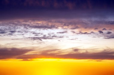 Derinleşen mavi arka planda altın ve ateşli bulutların yer aldığı dramatik bir gün batımı gökyüzü. Zengin renkler ve dinamik bulut oluşumları çarpıcı bir doğal görüntü yaratır..