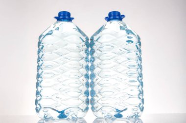 Mavi kapaklı iki plastik su şişesi ve beyaz arka planda izole edilmiş eşsiz dalgalı bir tasarım. Sağlık, hidrasyon veya ekolojik bilinçli ürün hisse senedi tasviri için uygundur..