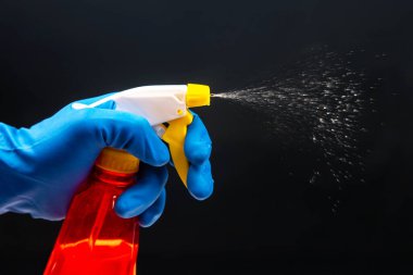 A gloved hand activates a red spray bottle with a yellow nozzle, releasing a fine mist on a black backdrop, perfect for cleaning product ads or sanitation themes.