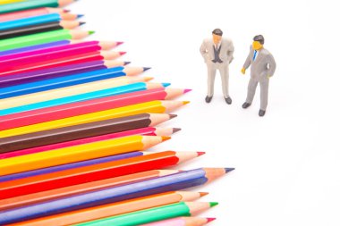 Beyaz bir yüzeye yayılmış renkli kalemler, ayakta duran minyatür işadamları, sanatsal ifade ile kurumsal tasvirleri birleştiriyor. minyatür insanlar