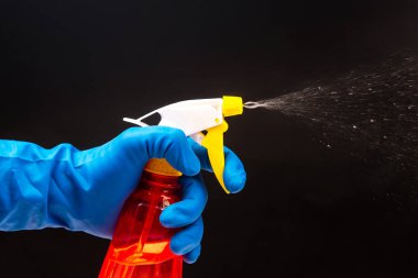 blue-gloved hand using a red spray bottle with a yellow trigger, mist in motion against a dark background, great for household cleaning or safety visuals.