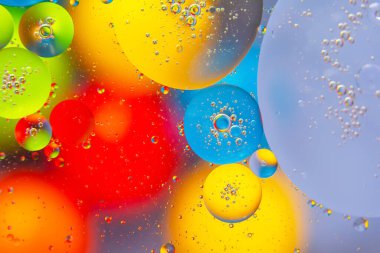 Pürüzsüz bir zemin üzerinde parlak kırmızı, sarı, mavi ve yeşil tonlarda su damlalarının çarpıcı soyut bir görüntüsü..