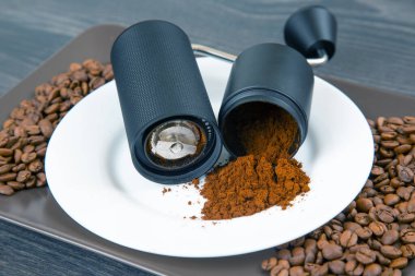 Manüel kahve öğütücüsünün detaylı görüntüsü, taze öğütülmüş kahveyi ortaya çıkarmak için bölünmüş, beyaz bir yüzeyde küçük bir toz damlası, kahve hazırlama üzerine vurgu yapıyor..