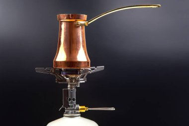 Pirinç saplı parlak bakır bir Türk kahve demliği, portatif bir gaz sobasının üzerinde beyaz bir gaz tenekesinin üzerinde, parlak, koyu bir zemin üzerine kurulmuş, kahve demlemek için mükemmel.