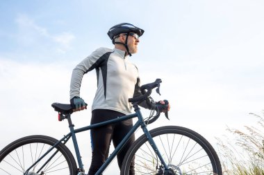 Sakallı adam bisikletçi mavi gökyüzüne karşı bir bisikletle duruyor. bisiklet ve sağlık hobileri