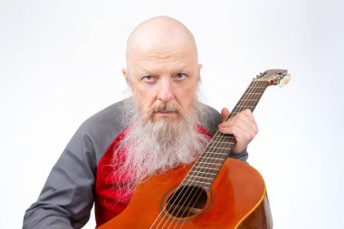 Uzun gri sakallı yaşlı bir adam, kırmızı ve gri spor gömlekli tahta bir gitarla beyaz bir arka plana karşı şarkı söylüyor ve müziğe olan sevgisini vurguluyor..