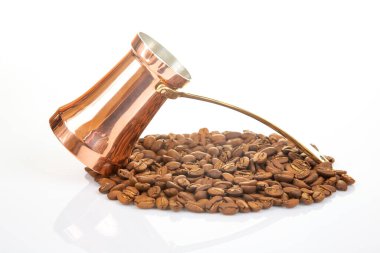 Beyaz bir yüzeye yayılmış kahve çekirdeğinin yanında pirinç saplı otantik bakır kahve demliği, kültürel miras ve içecek fotoğrafçılığı için mükemmel.