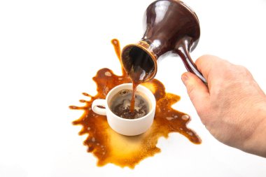 Kahve, zarif bir tencereden beyaz bir fincana dökülen bir el gibi taşar, beyaz yüzeye yayılan canlı bir sıçrama, dinamik ve tesadüfi bir anı gösterir..