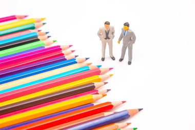 Beyaz bir yüzeye yayılmış renkli kalemler, ayakta duran minyatür işadamları, sanatsal ifade ile kurumsal tasvirleri birleştiriyor. minyatür insanlar