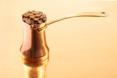 Altın bir yüzey üzerinde kahve çekirdeği yığını ile birlikte pirinç saplı cilalı bakır bir mağara, geleneksel kahve demleme ve yaşam tarzı temaları için mükemmel.