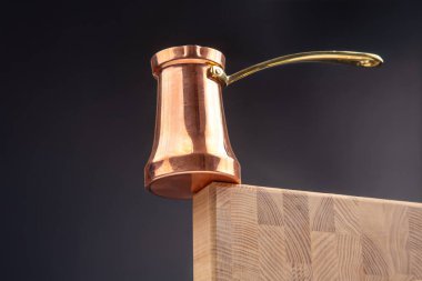 Ahşap bir bloğa tünemiş altın saplı geleneksel bakır bir mağara. Parlak, koyu bir zemin üzerine kurulmuş. Mutfak ve kültür fotoğrafçılığı için mükemmel.