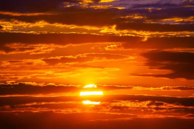 Güneş karanlık bir bulutun ardında batar, gökyüzünde altın bir parıltı bırakır. Aydınlatılmış bulut kenarları ve derin tonlar sahneye gizem ve güzellik katıyor..