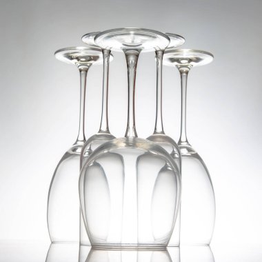 Zarif sapları düzgün sıralanmış, parlak bir masaya yansıyan zarif boş şarap kadehleri sofistike dekorlar için minimalist gri bir zemin üzerine kurulmuş..