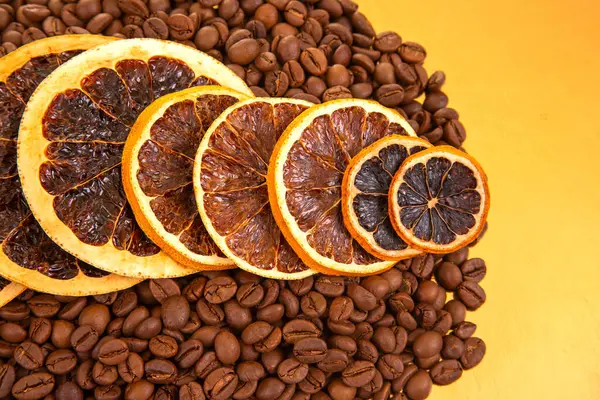 Kurutulmuş portakal dilimleri ve altın bir arka planda kavrulmuş kahve çekirdekleri, bir sabah içeceği sahnesinin sıcaklığını yansıtıyor. Kahve aroması ve turunçgiller.