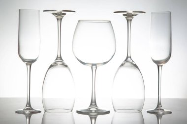 Uzun saplı beş zarif, boş şarap kadehinden oluşan gösterişli bir sıra yumuşak gri arka planda parlak bir yüzeye yansıyor. Yemek ya da etkinlik temaları için mükemmel..