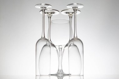 Kristal şarap kadehleri çeşitli şekillerde dimdik durur, yansımaları parlak bir yüzeyde ikiye katlanır, güzel yemek kavramları için yumuşak gri bir zemin üzerine yakalanır..