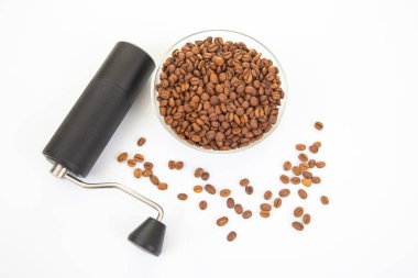 Siyah desenli kahve öğütücüsü ve metal sapı olan gösterişli bir el yapımı kahve öğütücüsü kavrulmuş kahve çekirdekleri ile dolu bir cam kasenin yanında duruyor..