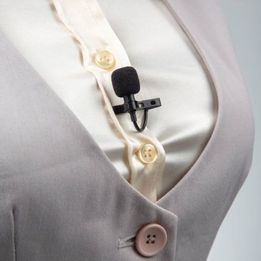 Krem rengi düğmeli bir gömleğe klipsli siyah bir lavalier mikrofon iliştirilmiştir, bu kayıt veya halka açık konuşma senaryoları için idealdir.