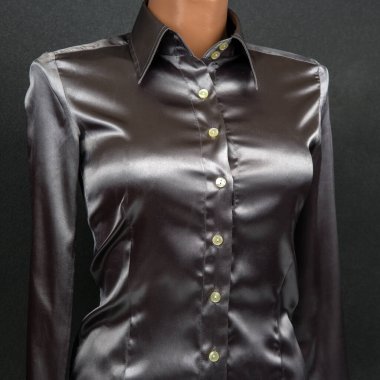 Siyah saten bir gömlek klasik bir tasma ve önü düğmeli bir gömleğe sahiptir. Bir mankende gösterilen kumaş ışığı yansıtır ve stüdyo ortamındaki koyu bir arka planda zarif bir görünüm oluşturur..