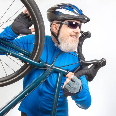 Mavi ceketli ve kasklı bir bisikletçi elinde bisiklet tutarken gülümsüyor. Bisiklet dükkanında, maceraya hazır, bisiklet ve spor yapma tutkusu sergiliyor..