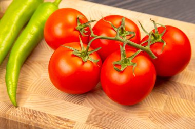 Parlak kırmızı domatesler, canlı yeşil biberlerle birlikte ahşap bir kesim tahtasının üzerinde otururlar. Taze ürünler, yemek hazırlıkları için sergilenir. Salatalar, soslar ya da mutfak kreasyonları için mükemmel..