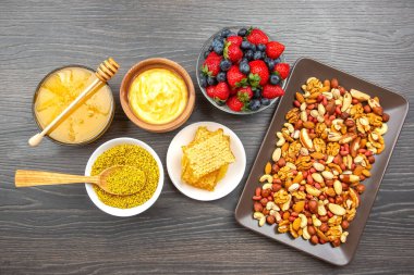 Ahşap bir yüzey üzerinde canlı bir abur cubur çeşidi düzenlenir. Buna çeşitli fındık, bal, taze çilek, yaban mersini ve kremalı sos da dahil. Besleyici bir ikram için mükemmel..