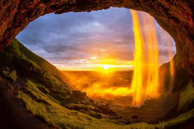 İzlanda 'daki Seljalandsfoss şelalesinden geçen muhteşem güneş ışığı manzarayı altın sarısı bir tonla aydınlatıyor. Canlı renkler günbatımında sakin atmosferle eşleşiyor.