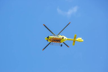 Açık mavi gökyüzünde belirgin çizgilere sahip parlak sarı bir helikopter, gün ışığının geniş zeminine karşı çevik tasarımını sergiliyor. Atmosfer sakin ve sakin..